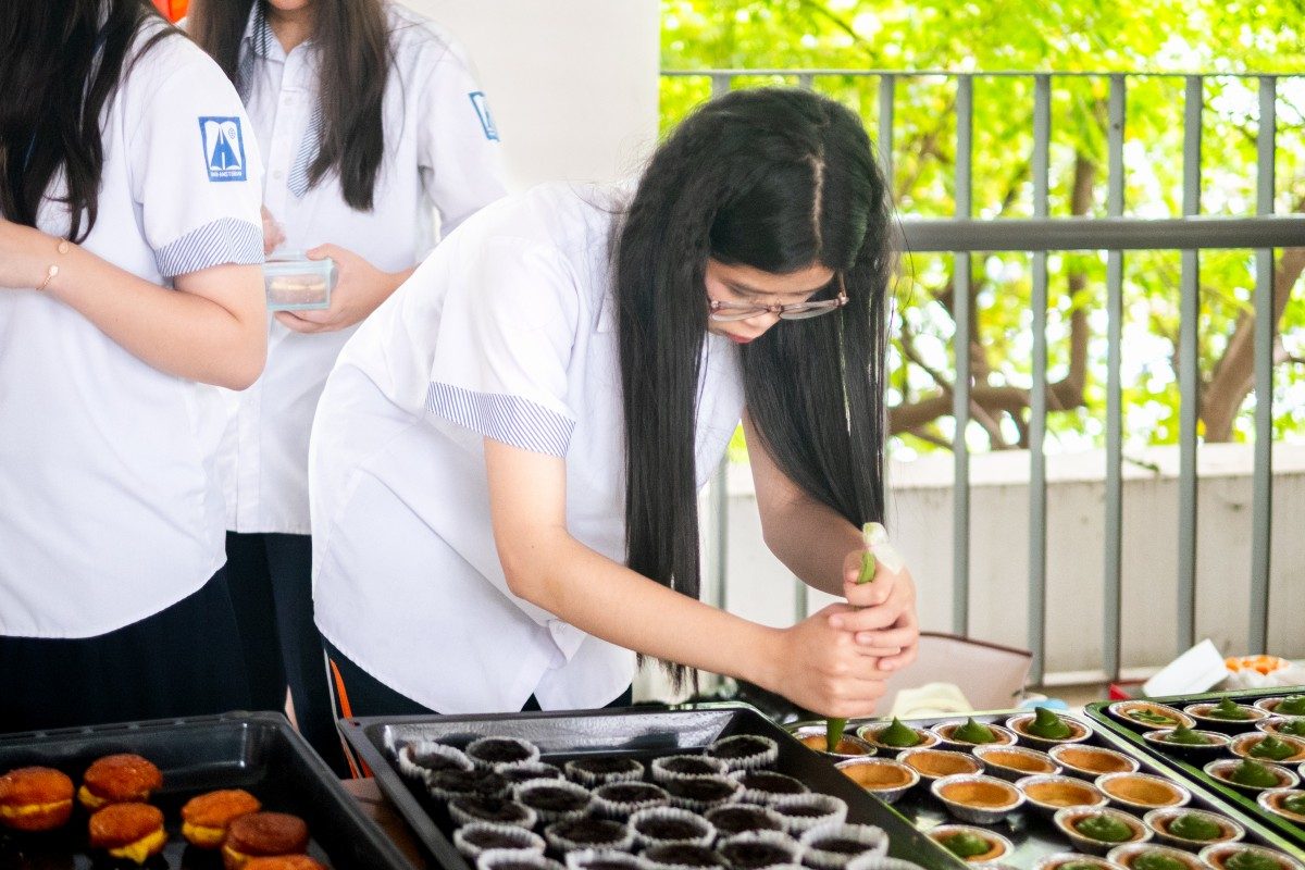 The students are diligently finishing the final steps to ensure the cakes reach customers in perfect shape.